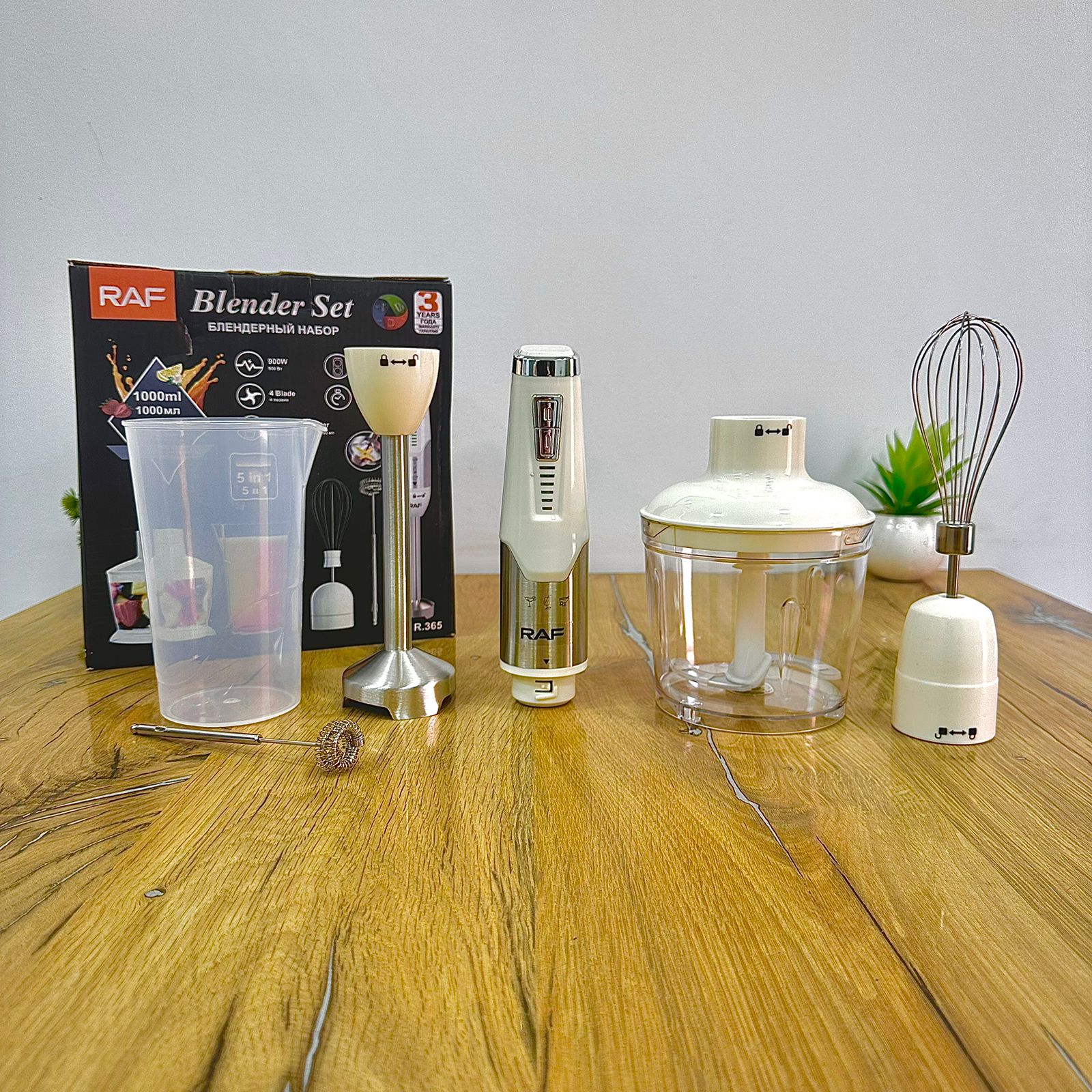 A 6-in-1 electric blender set by RAF, including a main blender jar, a hand blender, a food chopper attachment, a whisk, a clear measuring cup, and the original retail box, arranged on a wooden table against a plain wall.